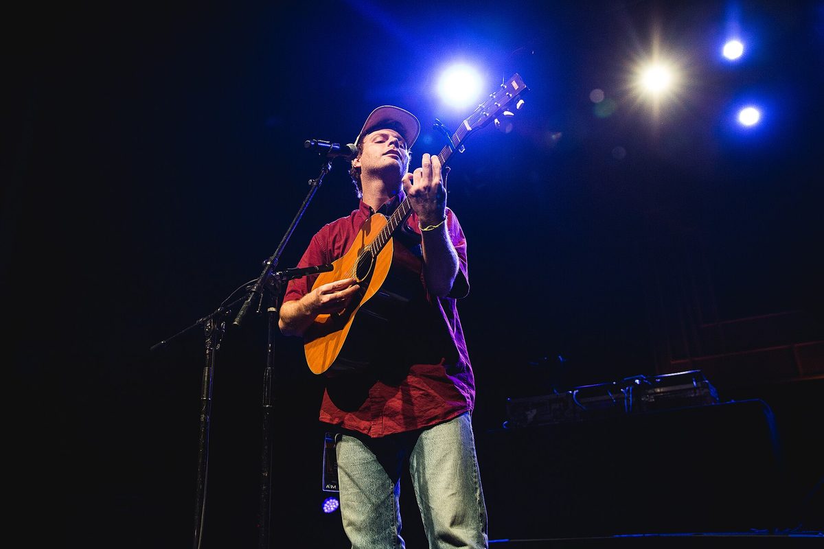 Mac DeMarco performing alone with an acoustic guitar under blue stage lighting at the 2016 A2IM Libera Awards.