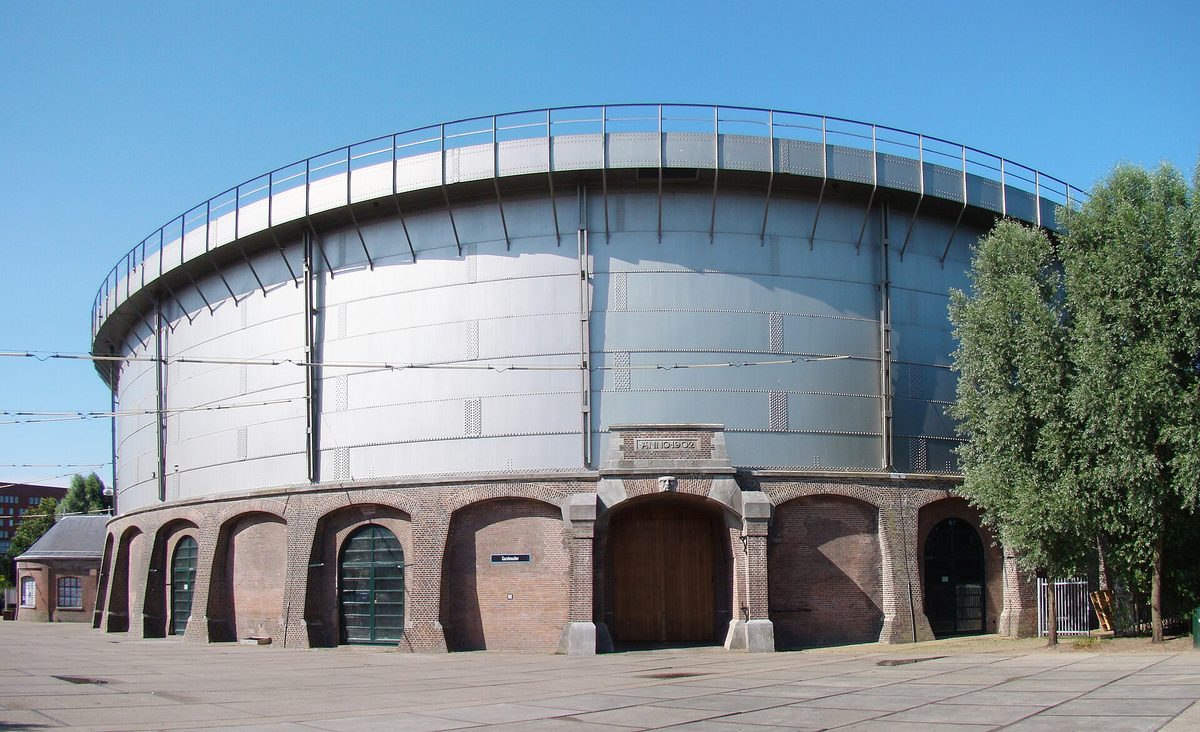 The circular brick and steel gasholder building at Westergasfabriek in Amsterdam, photographed from the courtyard on a clear day.