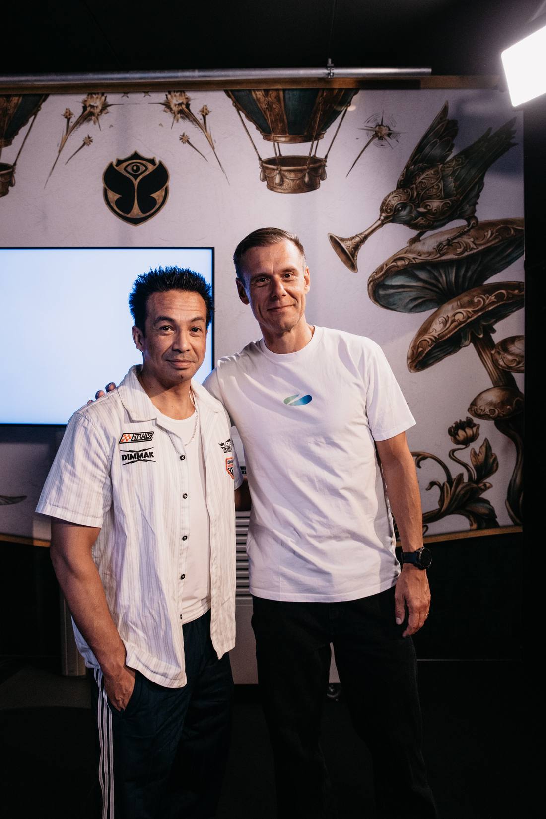 Laidback Luke and Armin van Buuren standing together backstage in front of Tomorrowland artwork