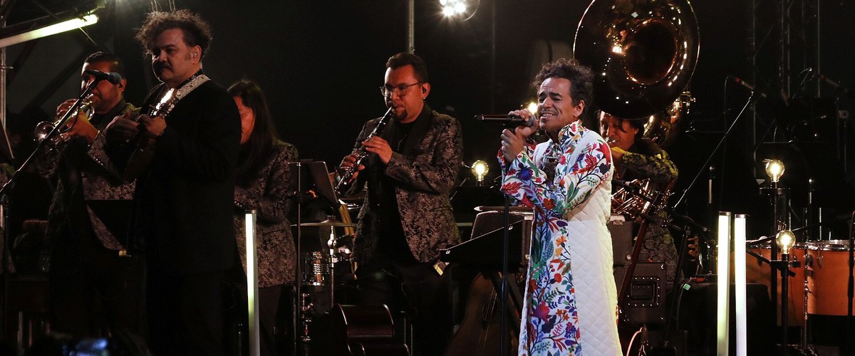 Café Tacvba's singer performing in a floral coat with the band and a brass section on stage
