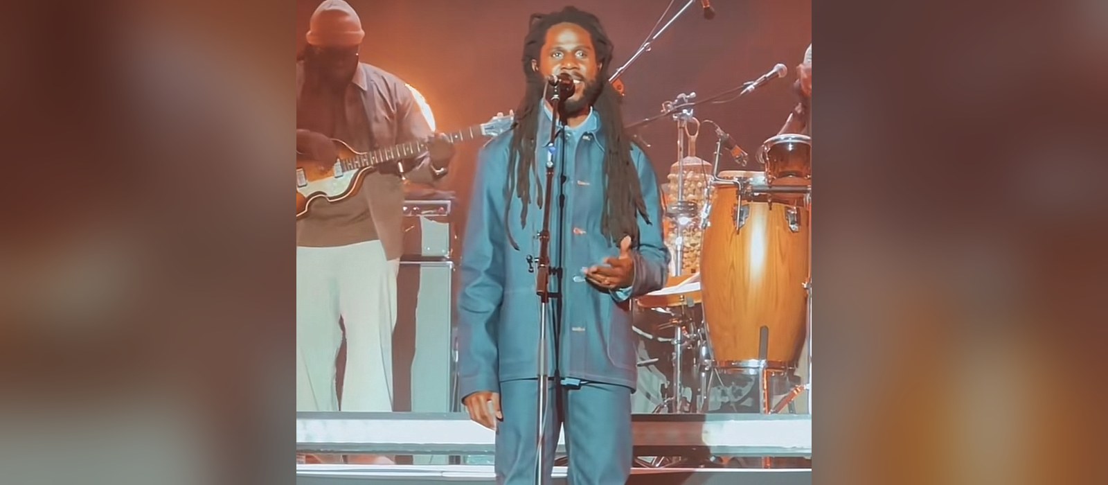 Chronixx singing into a microphone at Reggaeland 2025, with his live band playing behind him