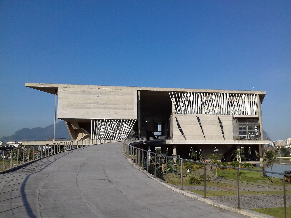 Cidade das Artes in Barra da Tijuca, a raised concrete building with deep horizontal slabs and a slatted screen facade, seen from its approach ramp.