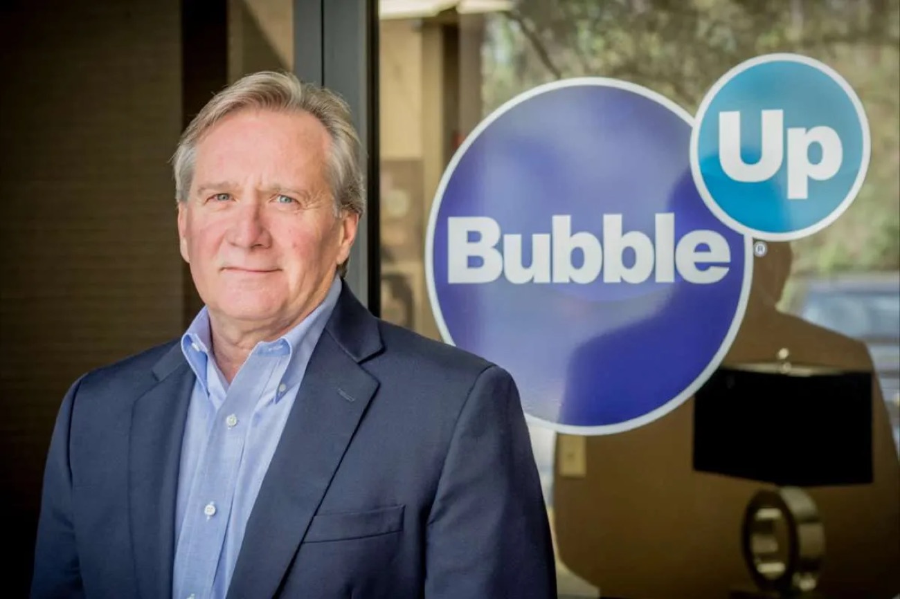 Coleman Sisson, CEO of BubbleUp, in a navy blazer standing beside the company's logo
