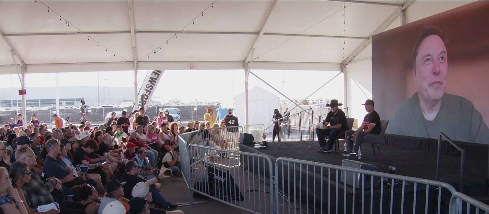 Elon Musk on a big screen in a tent at Giga Texas during his virtual X Takeover 2026 interview