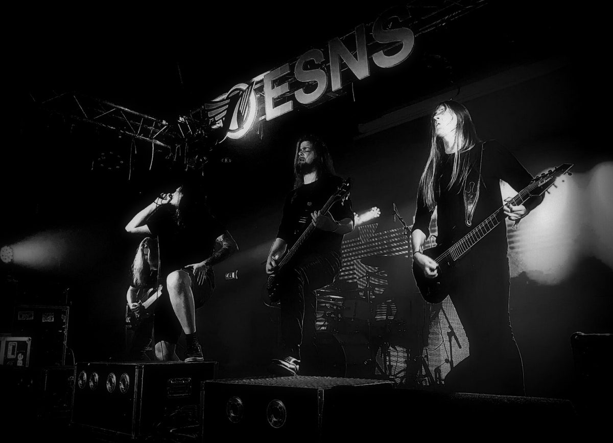 A band performing under a large illuminated ESNS sign, shot in black and white, the singer leaning back mid-song.