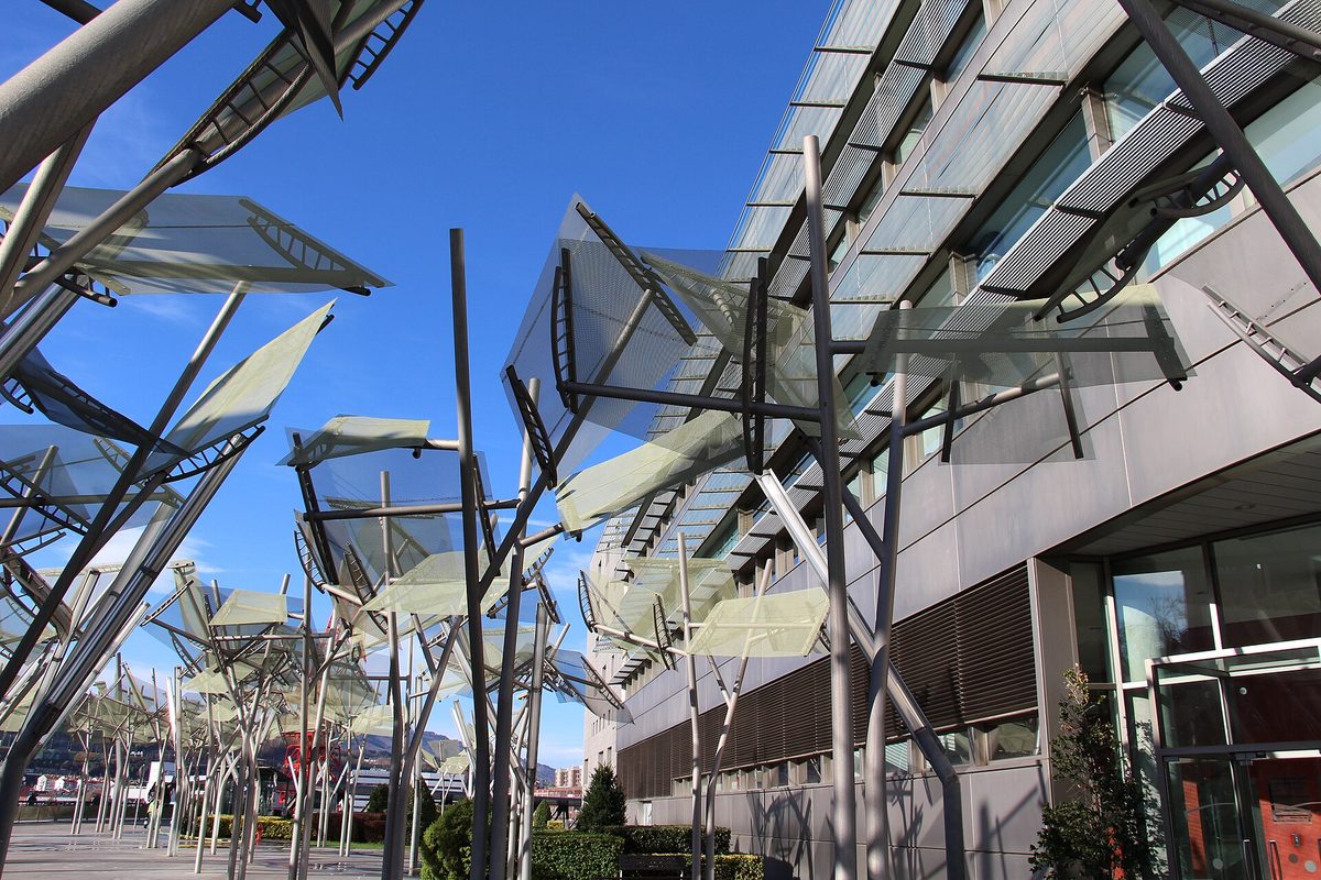 Looking up at the angular steel and glass canopies outside the Euskalduna Palace against a clear blue sky.