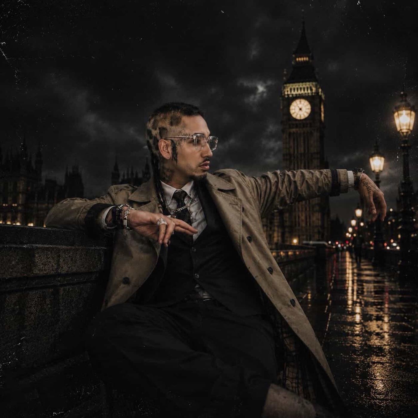 Fenix Flexin in a trench coat and tie leaning on the parapet of Westminster Bridge at night, with Big Ben lit behind him