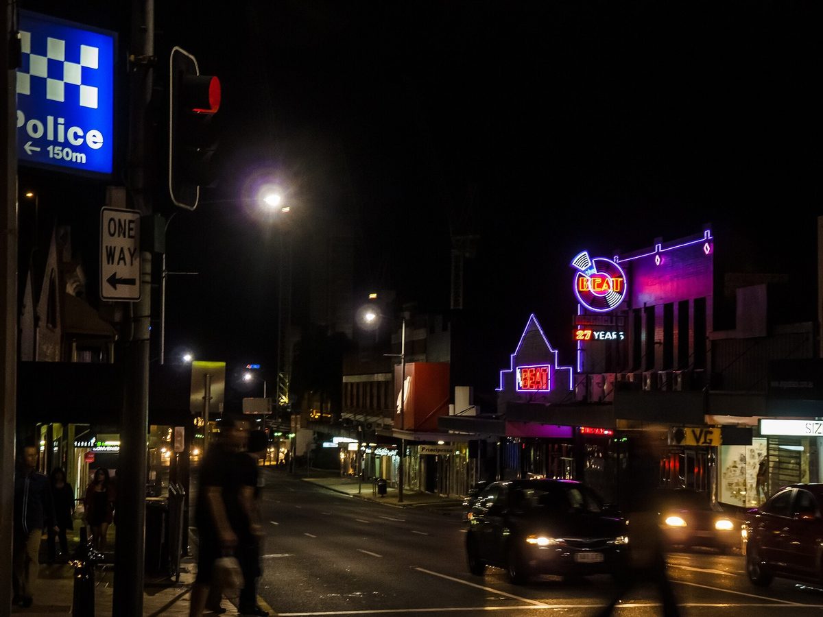 Neon signage outside The Beat nightclub on Ann Street in Fortitude Valley at night, with traffic passing on the wet road.