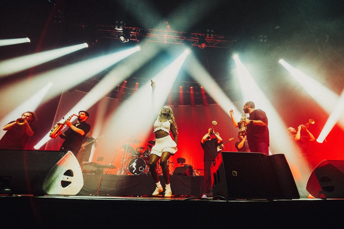 Band with a horn section performing on a large stage under bright spotlights at a live show