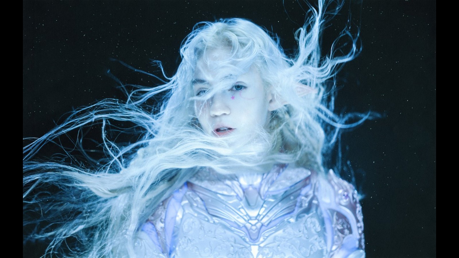 Grimes with long white windswept hair in a still from the Accelerando music video
