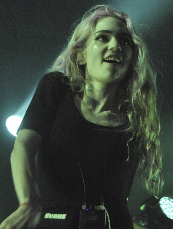 Grimes performing on stage at Governors Ball 2014, smiling, with long pastel-pink hair under stage lights.