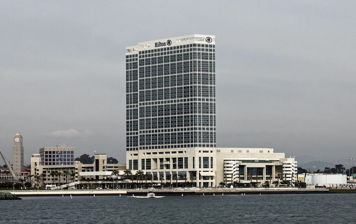 The Hilton San Diego Bayfront hotel, a tall glass tower on the waterfront, photographed across the bay on an overcast day.