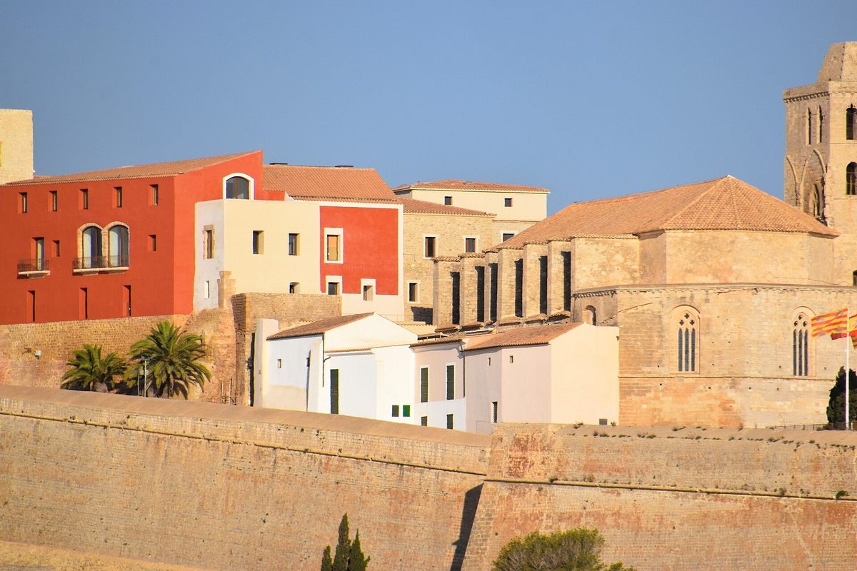 The historic walled city of Ibiza seen from the port, with terracotta and ochre buildings stacked above the fortified sandstone wall.