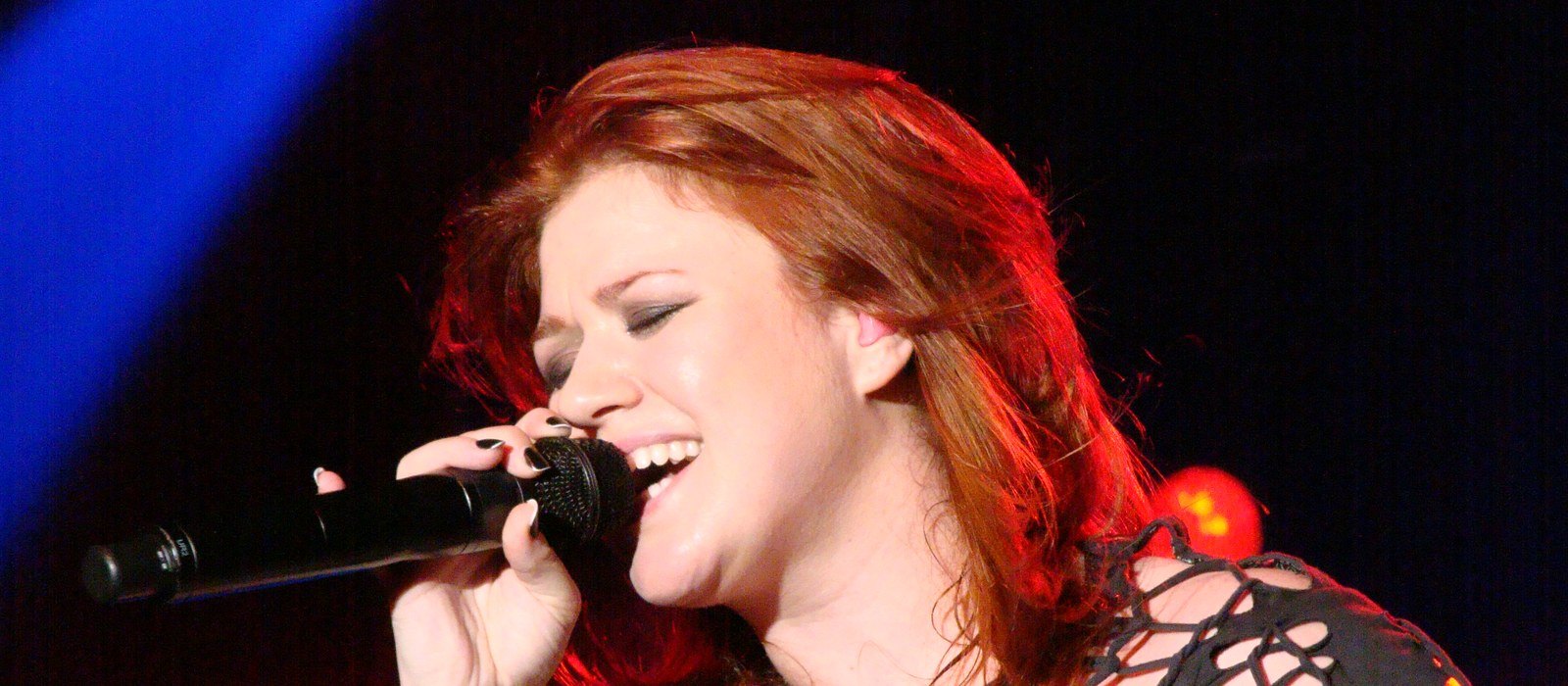Kelly Clarkson singing into a handheld microphone on stage at the Birmingham O2 Academy