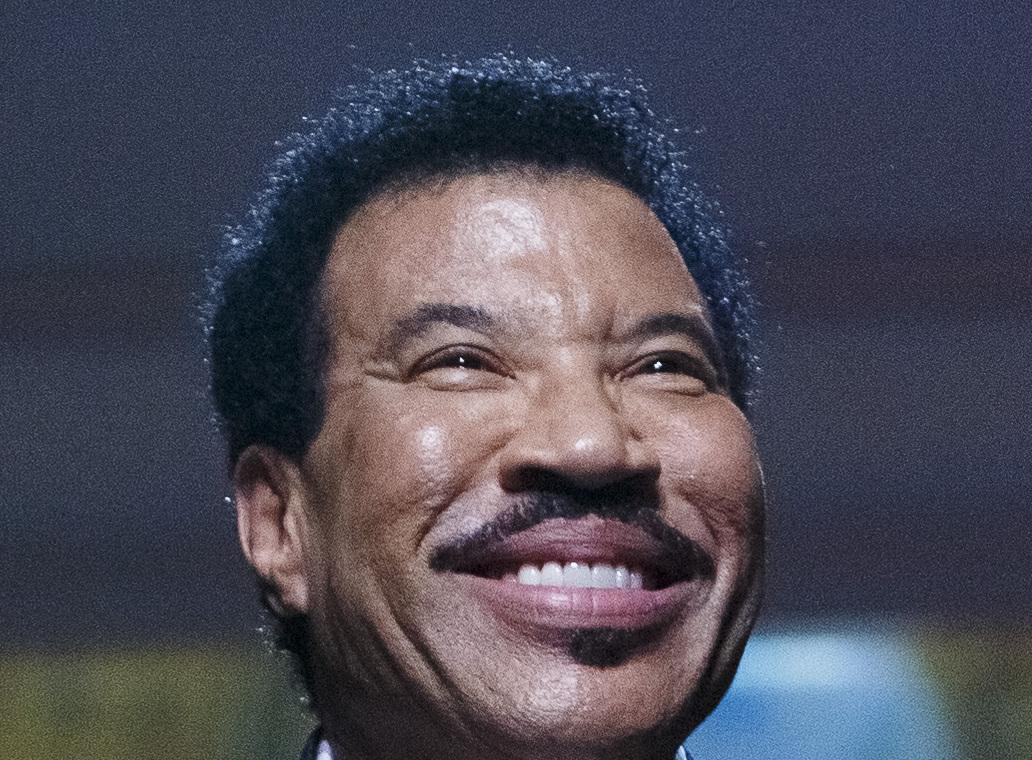 Lionel Richie smiling in close-up on a dark stage in 2022