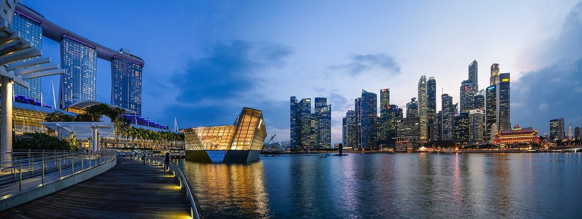 The Marina Bay waterfront in Singapore at dusk, the financial district towers lit against a deep blue sky and reflected in the water.