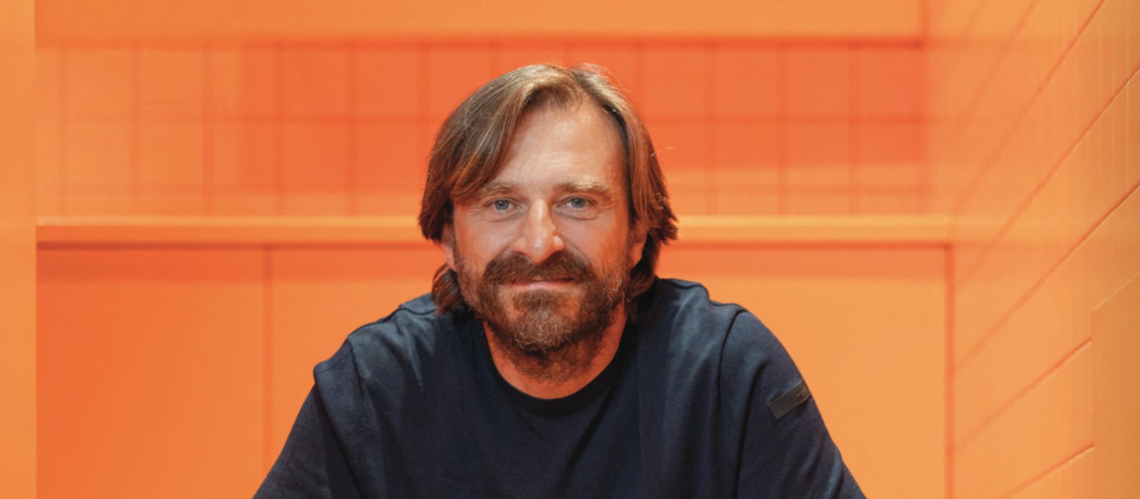 Musixmatch founder and CEO Max Ciociola seated in front of an orange wall, photographed for his MBW interview