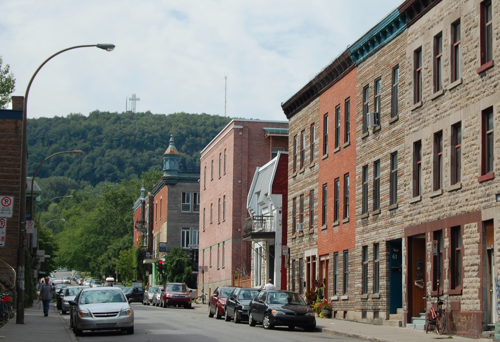 A residential street in the Plateau Mont-Royal district of Montreal, lined with brick and stone terraces, with the cross on Mount Royal visible on the hill behind.
