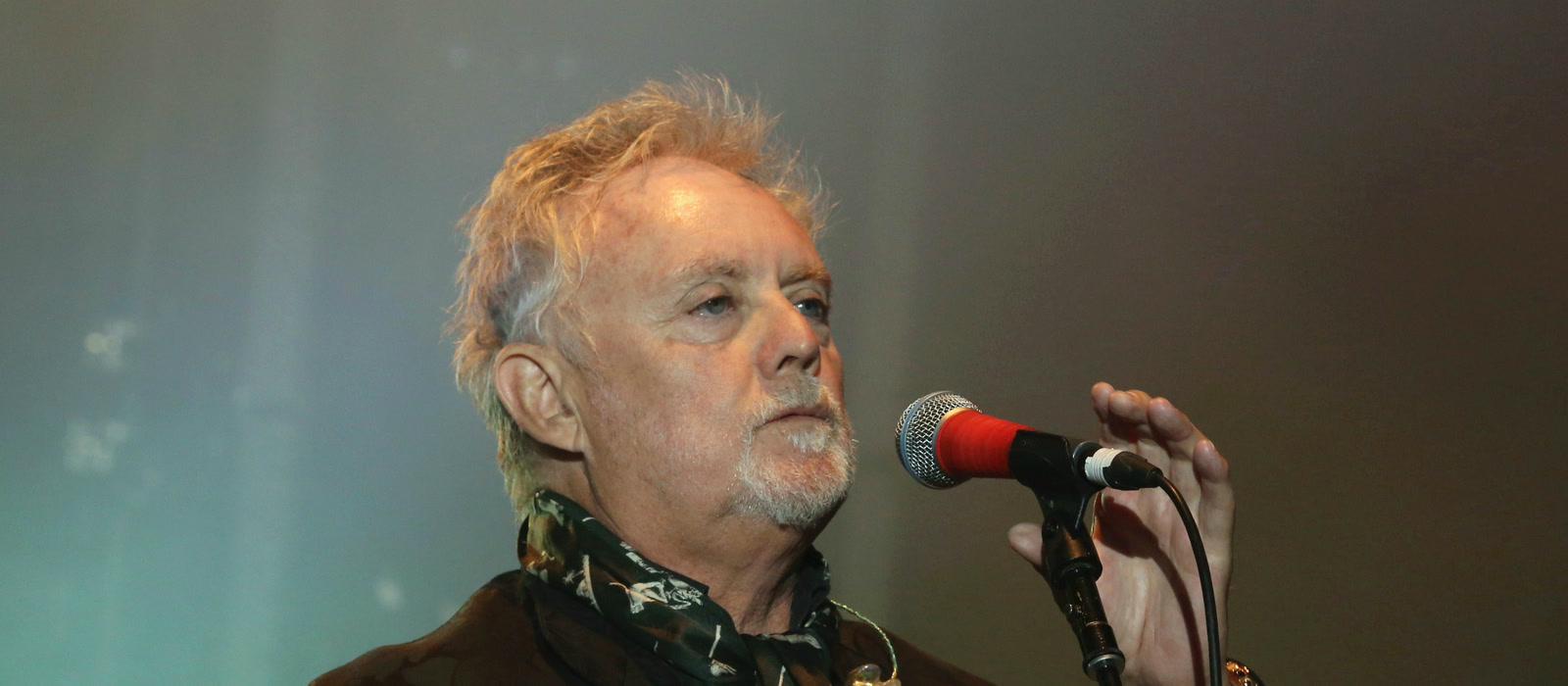Queen drummer Roger Taylor singing into a microphone on stage, pictured during a live performance