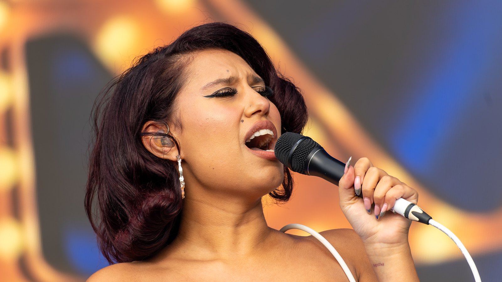Raye singing into a microphone on stage at Boardmasters Festival in Cornwall in 2023