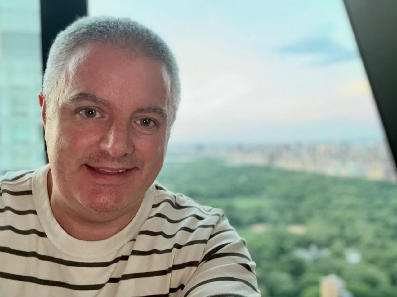 Musician Samuel Smith smiles in a striped shirt with the New York skyline and Central Park behind him