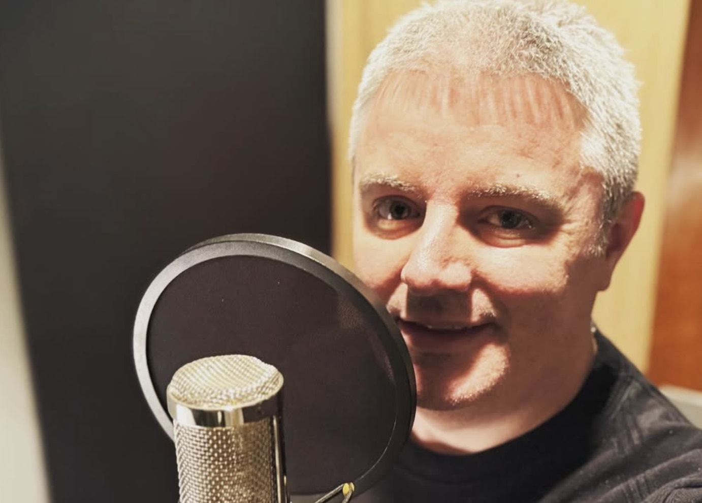 Samuel Smith smiles beside a studio microphone and pop filter during a vocal recording session