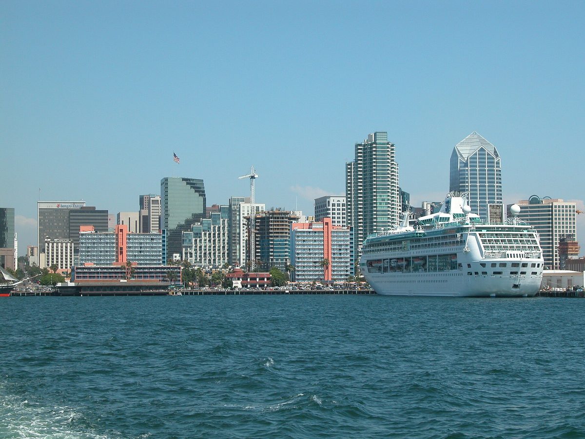 Downtown San Diego seen from the water on a clear day, with high-rise towers behind a moored white cruise ship.