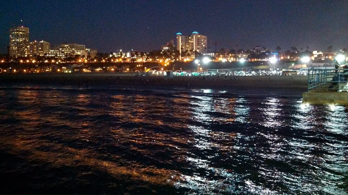 The lights of Santa Monica reflected across dark water at night, photographed from the end of the pier.