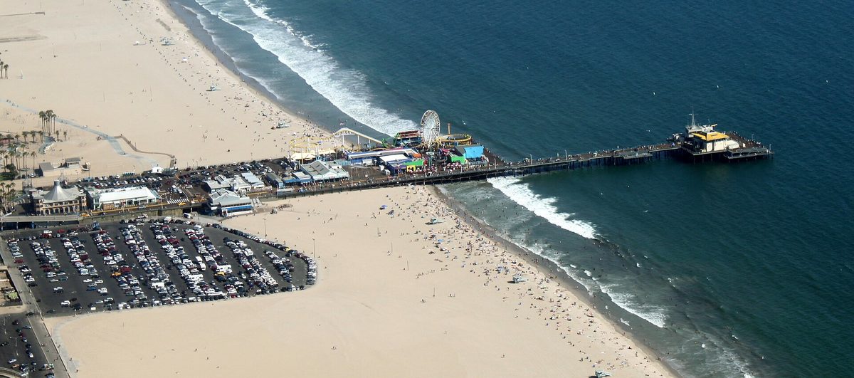 Aerial view of Santa Monica Pier extending into the Pacific, with the beach, car parks and shoreline visible along the coast.