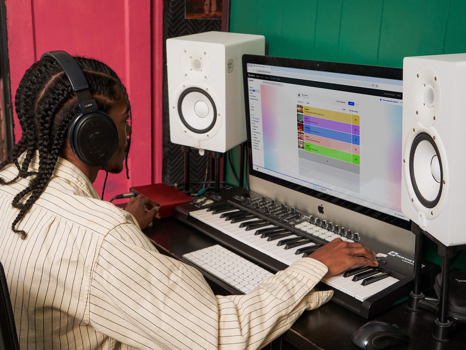 A producer using the Splice sample app on a studio computer with monitors and a MIDI keyboard