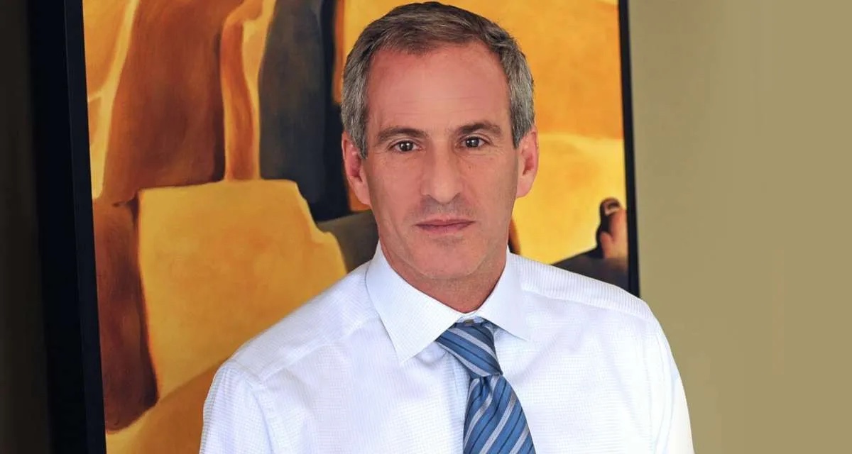 Steve Berman, Hagens Berman co-founder, in a white shirt and striped tie standing before an abstract painting