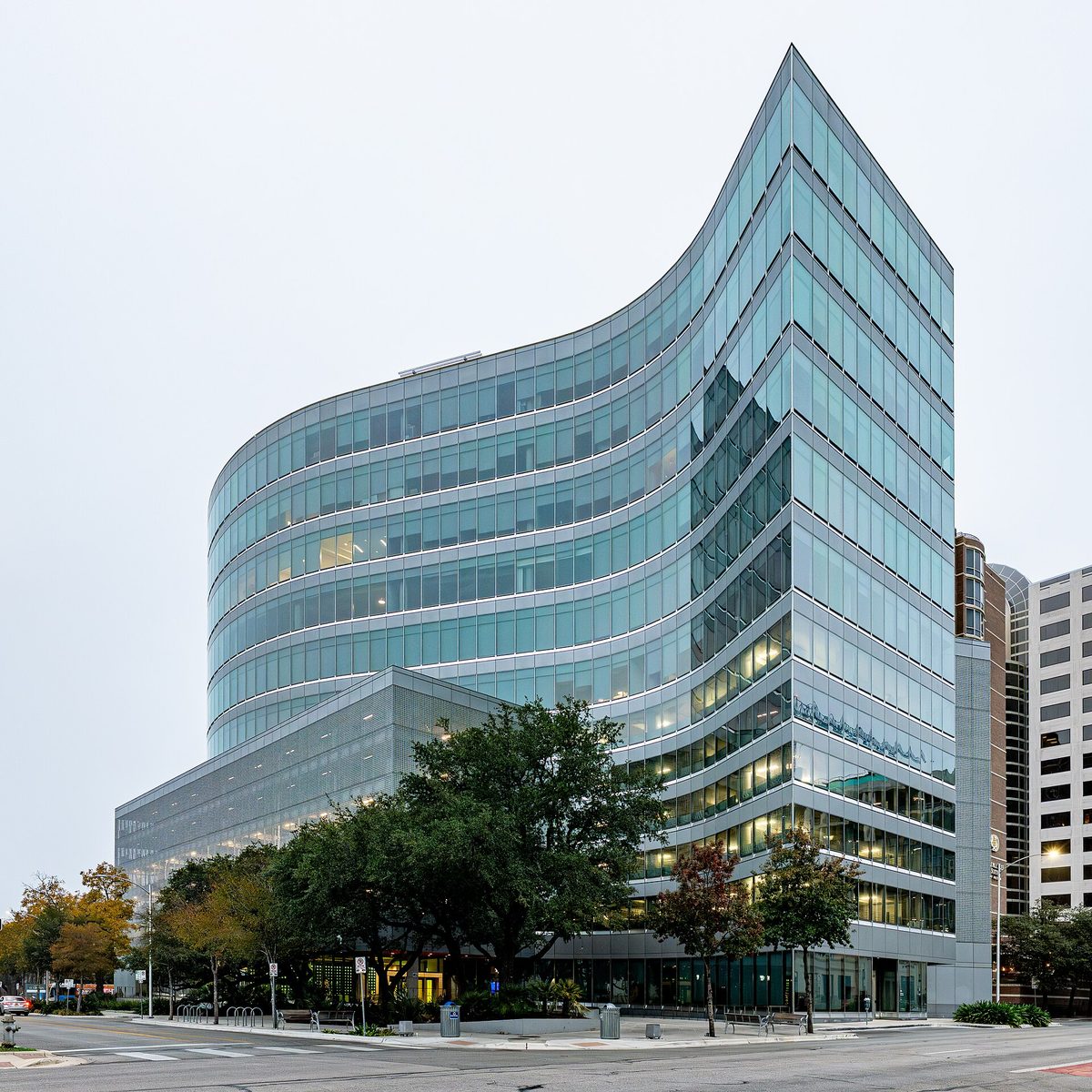 A curved glass office building in downtown Austin housing the SXSW Center, photographed from the street corner on an overcast day.