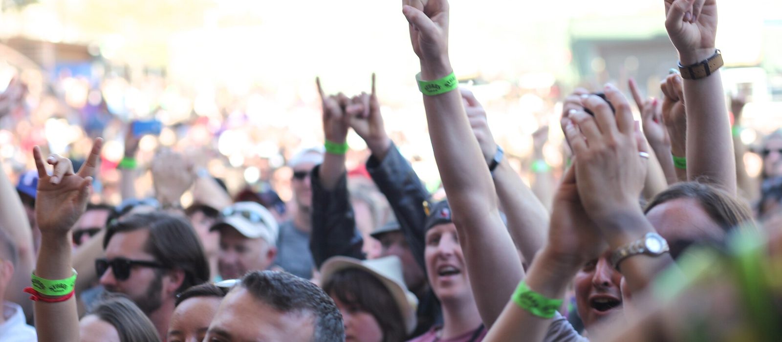 A dense outdoor crowd at SXSW with arms raised and hands making horn signs, green festival wristbands visible on several wrists.