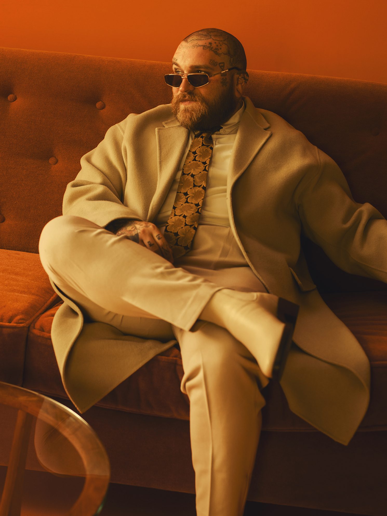 Teddy Swims in a cream suit and floral tie on an orange couch