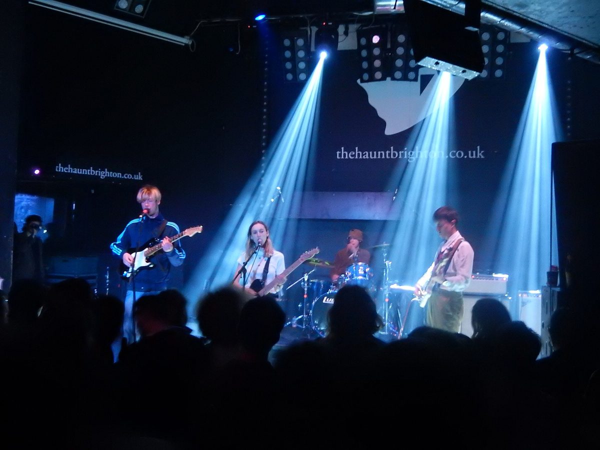 A band playing at The Haunt in Brighton, backlit by blue spotlights above a crowd of silhouetted heads.