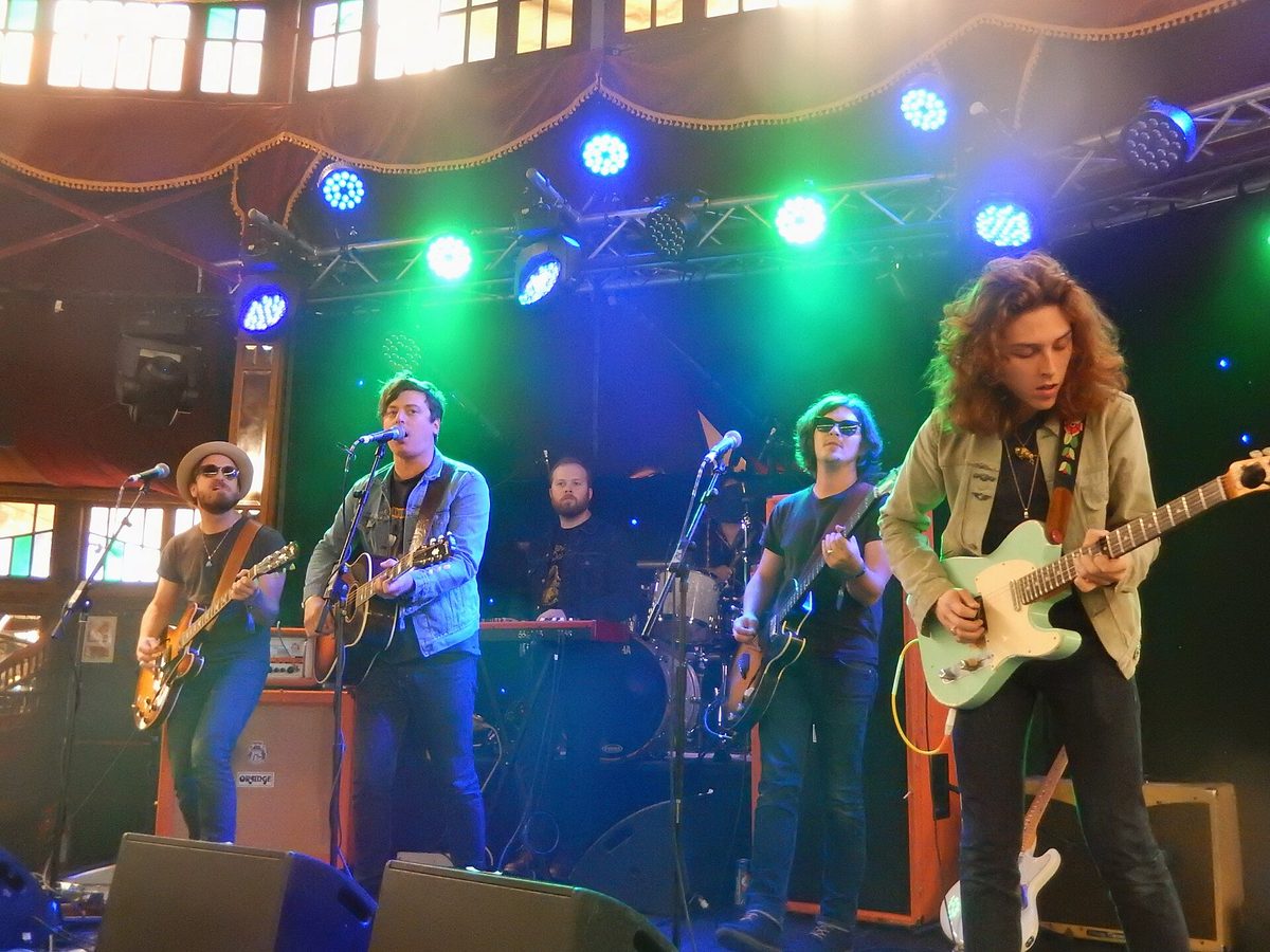 A five-piece band performing on a small stage under green and blue lighting inside the Spiegeltent at The Great Escape.