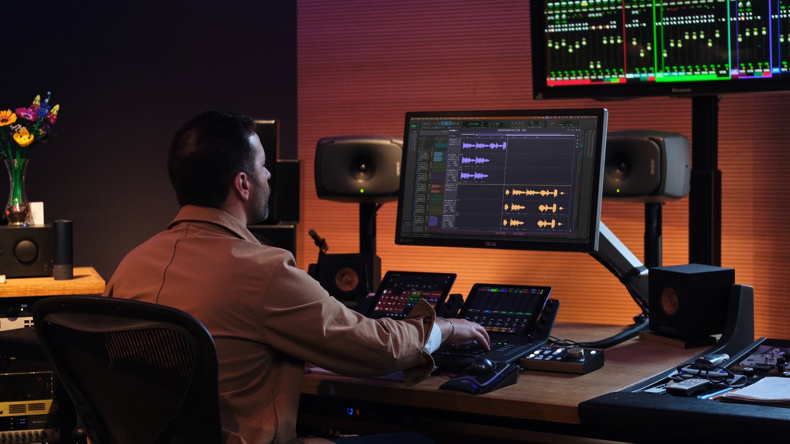 Producer at a studio desk editing a vocal stack in VocAlign 7 on a large monitor