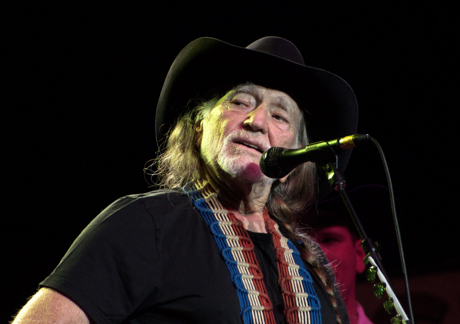 Willie Nelson singing into a microphone on stage in a black cowboy hat, one of the country artists opposing AI data centers