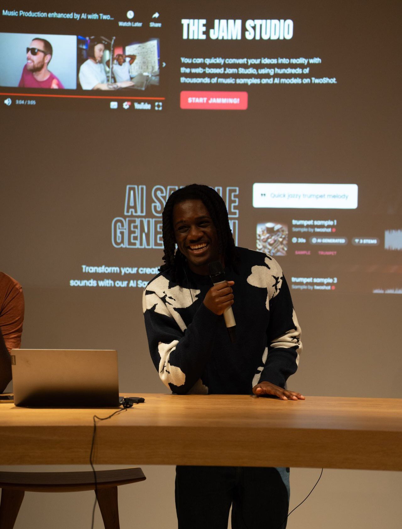 Twoshot founder Tobi Akinyemi smiling with a microphone in front of a Jam Studio product slide