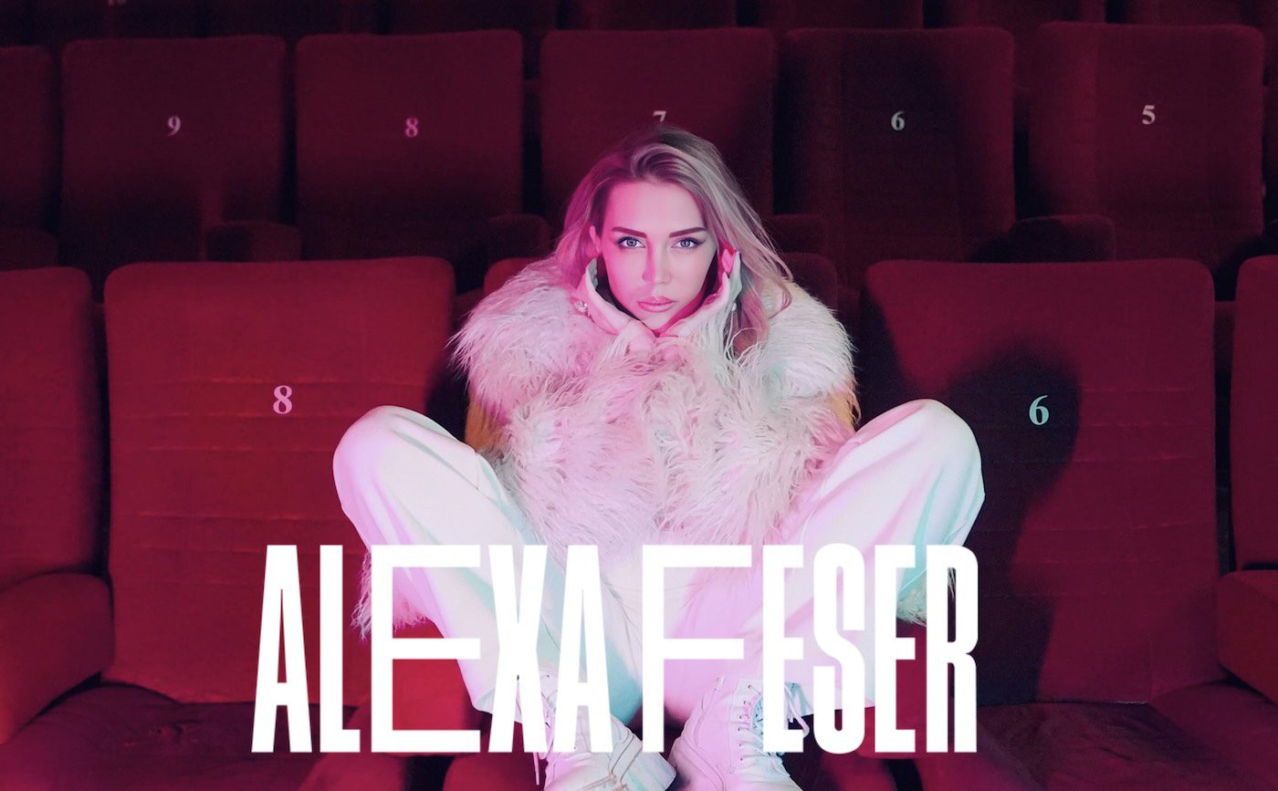 Alexa Feser sitting in a theater wearing a fur coat, with her name displayed in bold text below.