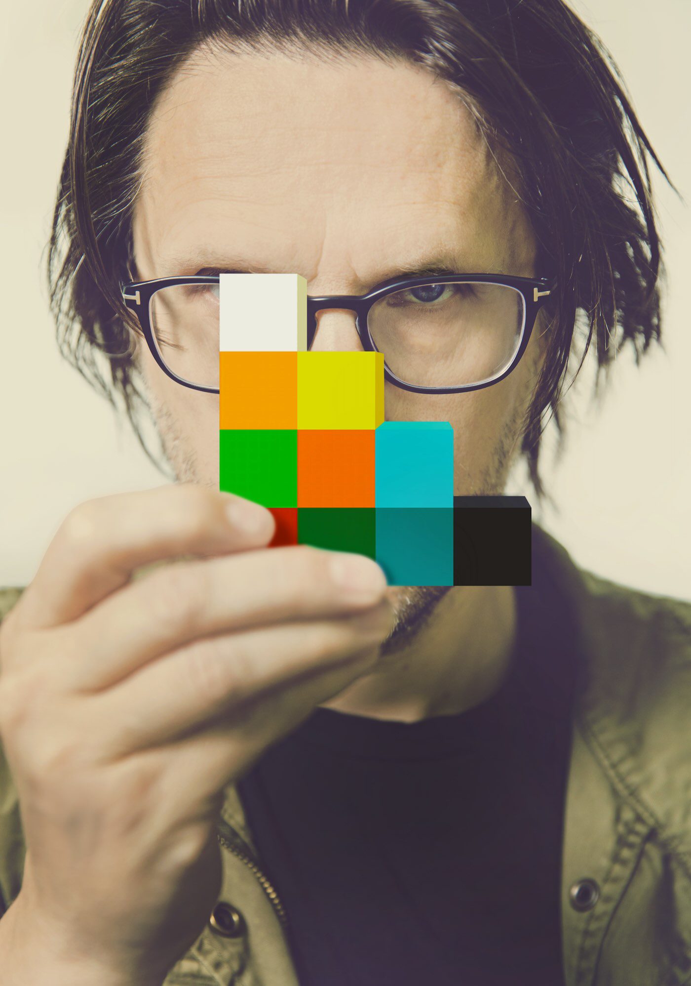 Steven Wilson with Blocks – Steven Wilson holds colorful stacked blocks, staring through glasses.