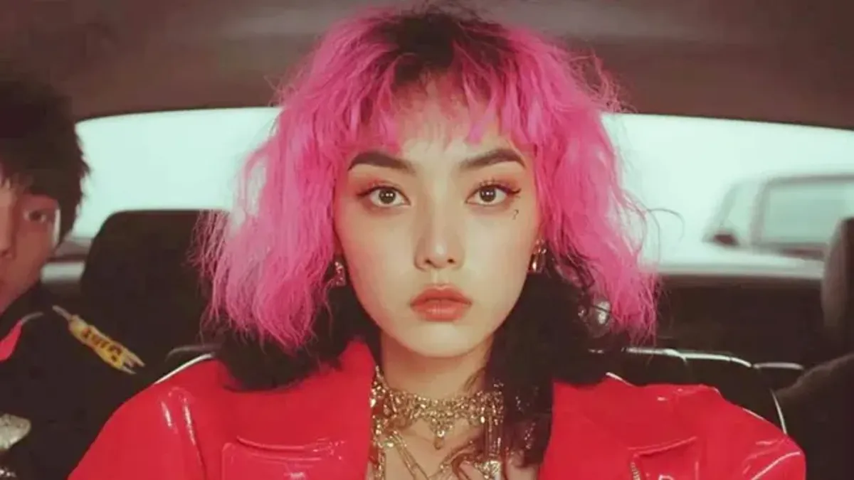 AI artist Tata in a red leather jacket and pink hair sitting in a car with gold chain jewelry