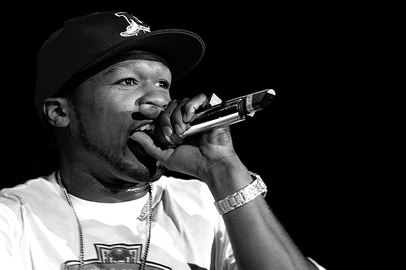 Black and white concert photo of rapper holding microphone with watch and chain, AI music topic.