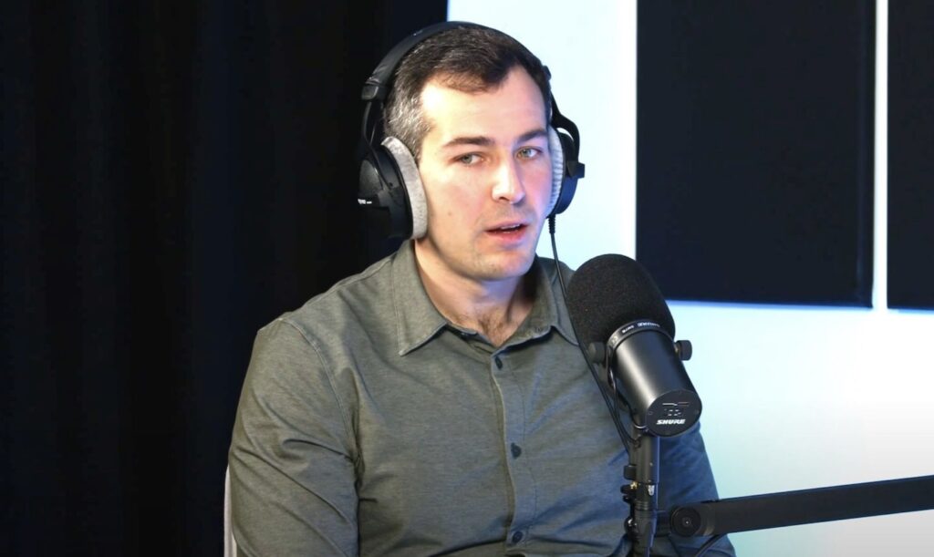 Mikey Shulman, CEO of Suno, wearing headphones speaks into Shure microphone during podcast recording.