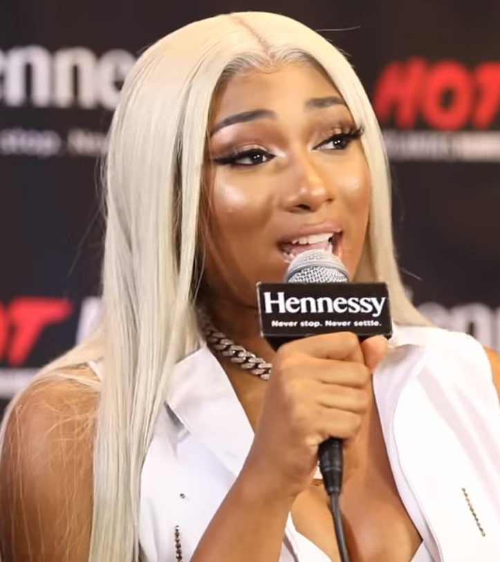 Megan Thee Stallion with platinum blonde hair speaking into Hennessy-branded microphone at event.
