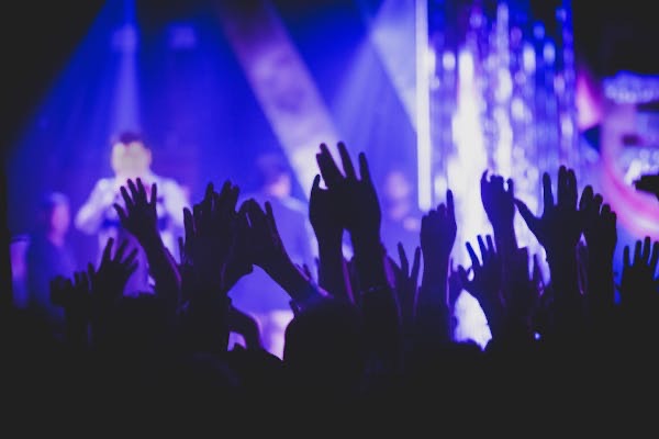 Concert crowd with hands raised in silhouette against blue and purple stage lights.