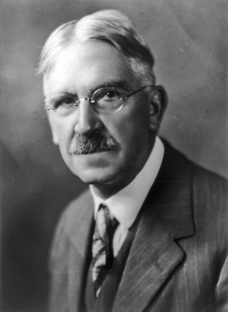 Black and white portrait of philosopher John Dewey wearing round glasses and a suit.