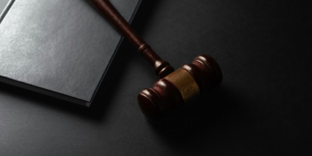 Wooden judge's gavel resting on a black hardcover book on a dark surface.