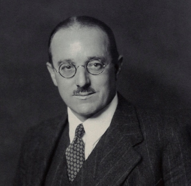 Black and white portrait of philosopher R.G. Collingwood in a suit with round glasses.