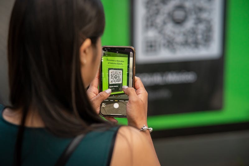 Woman scanning a Spotify EQUAL QR code on a large green billboard with her smartphone.